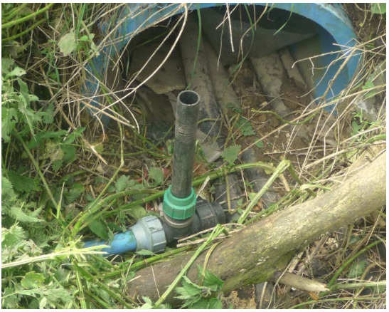 Photo of pipes and fittings at a private supply. Pipes are open, outside in grass, and disappear into the undergrowth.